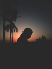 A nimble woman surrounded by vibrant buriti palms at sunset, the sky painted in warm orange and red hues reflecting the essence of the brand.