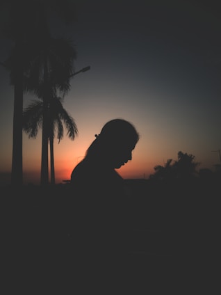 A nimble woman surrounded by vibrant buriti palms at sunset, the sky painted in warm orange and red hues reflecting the essence of the brand.
