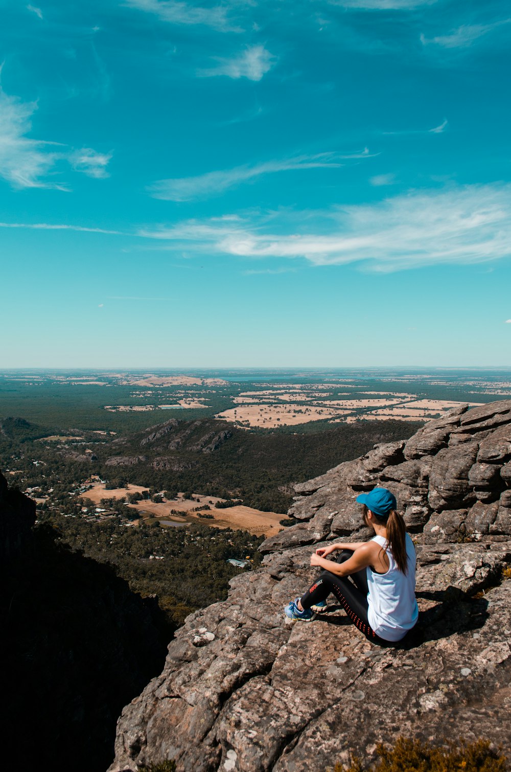 昼間の青空の下、崖の上に座る女性
