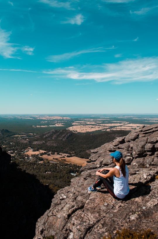 woman sitting on cliff under blue sky at daytime in Pinnacle Lookout Australia