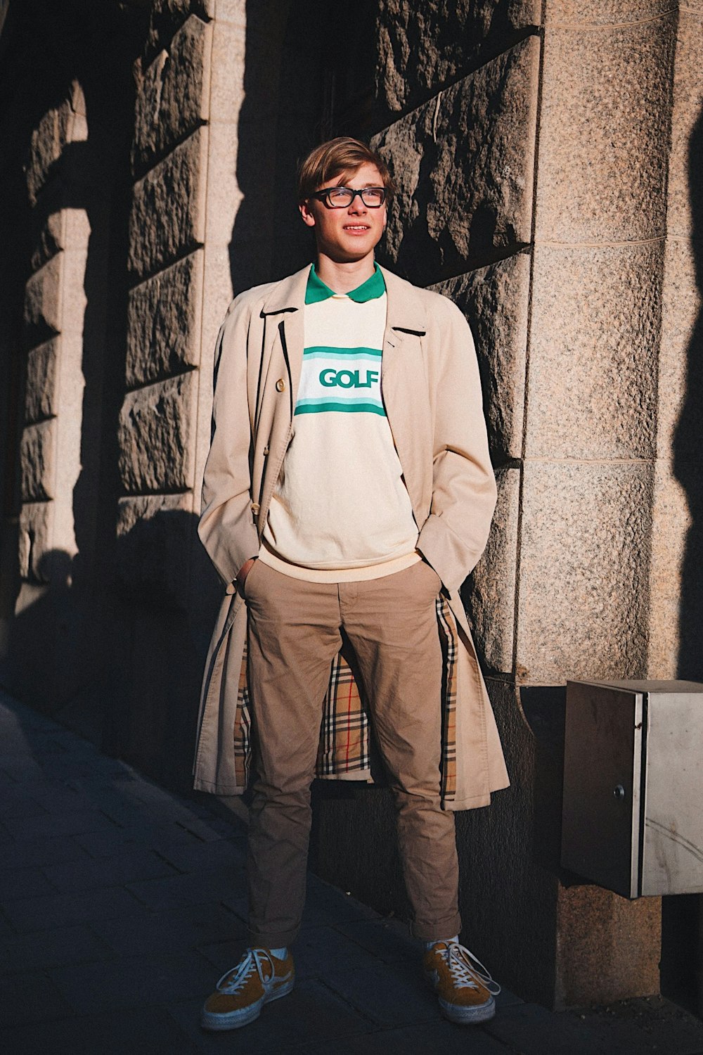 man in brown overcoat standing beside concrete wall