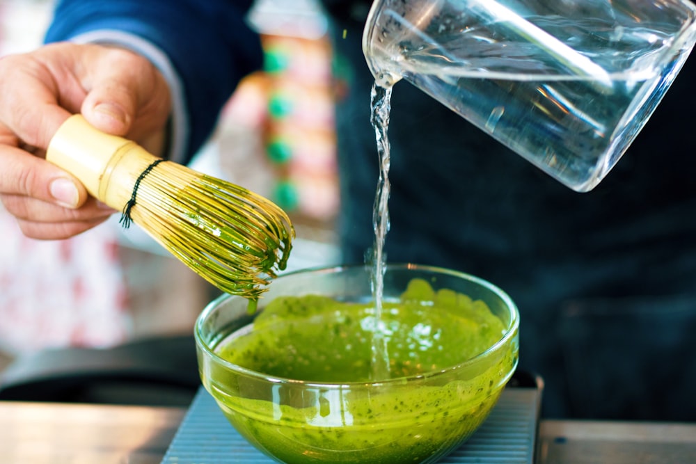 person pouring water into green sauce