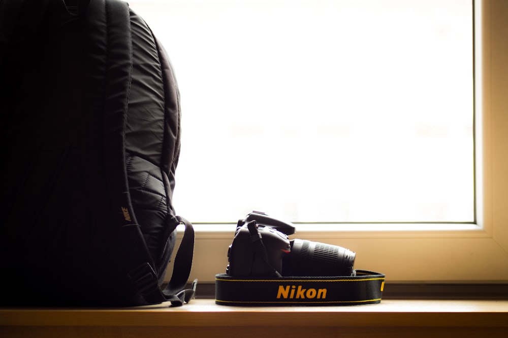 black Nikon DSLR camera beside black backpack