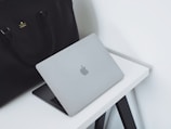 A sleek leather laptop bag resting on a wooden desk next to a laptop.