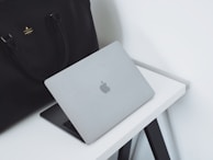 A laptop bag and accessories neatly arranged beside a laptop on a minimalist desk.