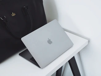 A sleek, modern corporate bag with a subtle embossed logo, resting on a wooden desk beside a laptop and coffee cup.