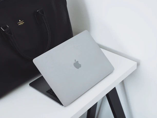 A sleek, modern corporate bag with a subtle embossed logo, resting on a wooden desk beside a laptop and coffee cup.