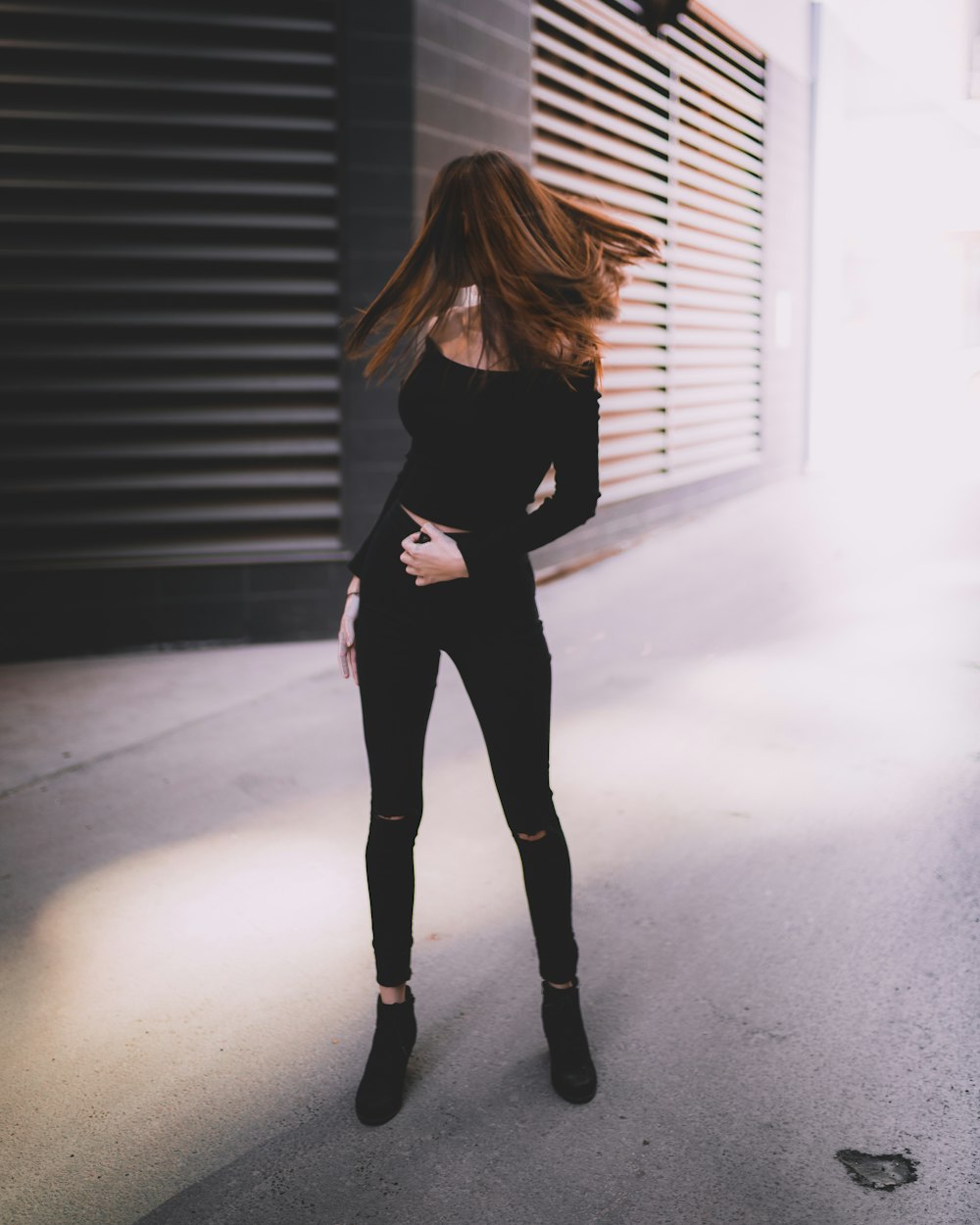 donna in top a maniche lunghe con spalle scoperte nere e pantaloni neri in piedi che ondeggiano i capelli