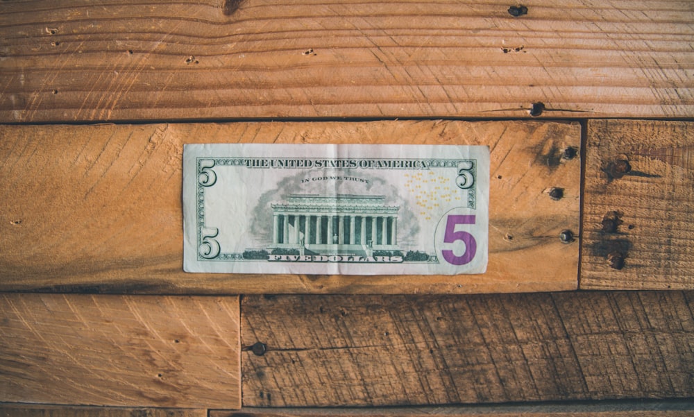 5 Dólar estadounidense sobre superficie de madera marrón