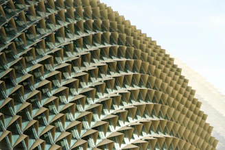 A close-up view of an architectural structure featuring a series of repeating triangular patterns. The geometric design creates a textured surface with triangular elements protruding outward, providing a striking visual effect.