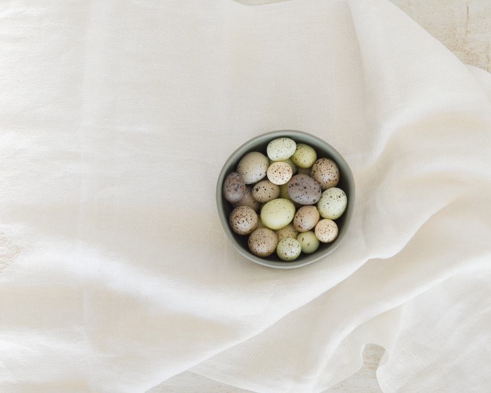 pebbles in gray ceramic bowl on white textile