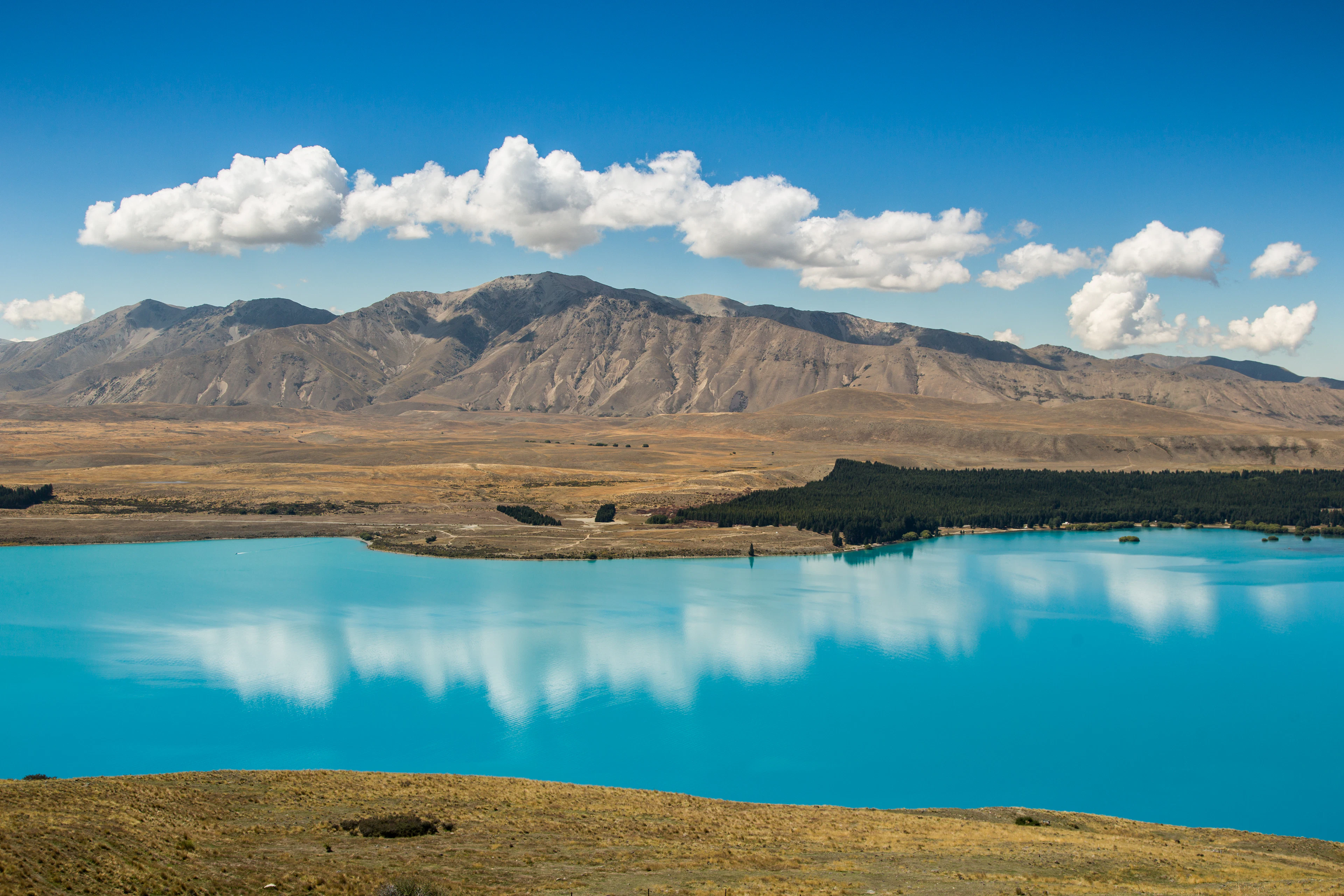 Turquoise Lake Tekapo reflecting clouds and brown hills, Canterbury, New Zealand