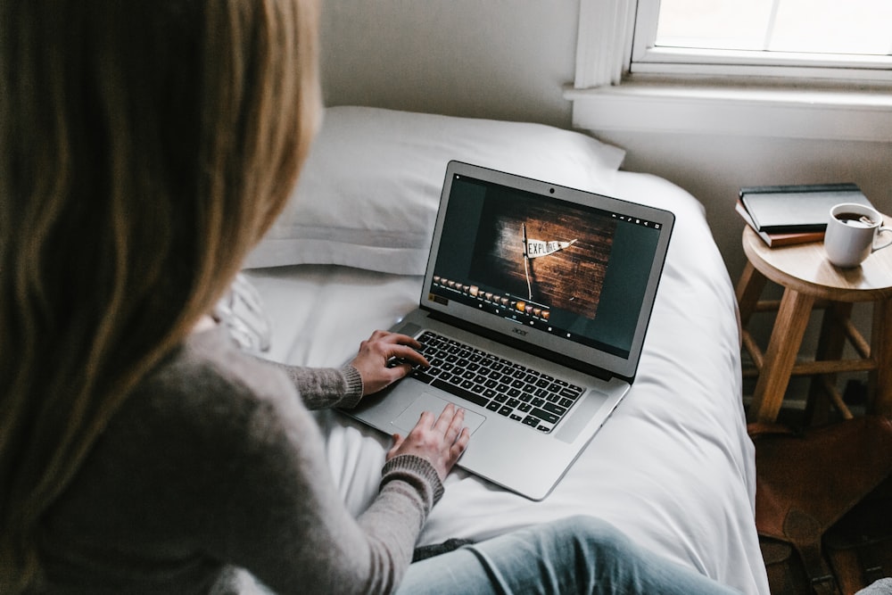 Frau benutzt grauen Laptop auf dem Bett