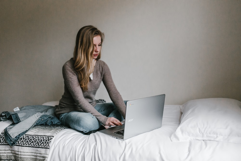 部屋のベッドに座ってMacBook Proでタイピングする女性