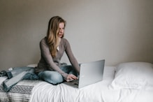 woman typing on MacBook Pro while sitting on bed in room