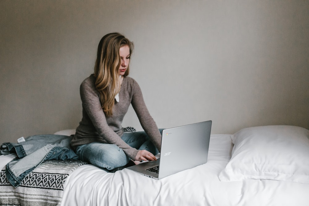 woman typing on MacBook Pro while sitting on bed in room
