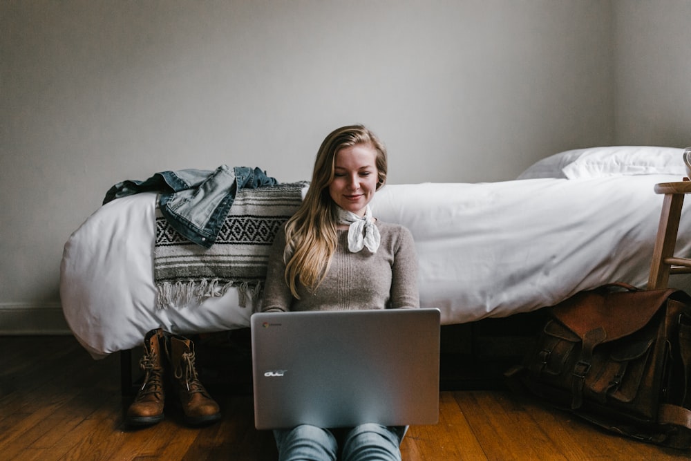 mulher sentada ao lado de uma cama enquanto usa um laptop