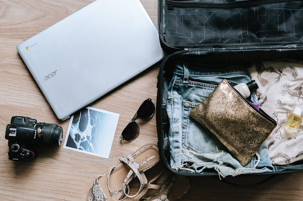 cámara DSLR negra cerca de gafas de sol y bolsa