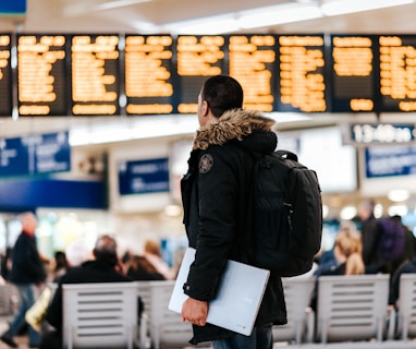 man standing inside airport looking at LED flight schedule bulletin board