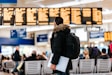man standing inside airport looking at LED flight schedule bulletin board