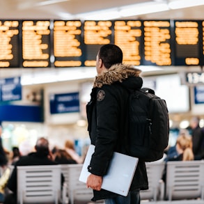 man standing inside airport looking at LED flight schedule bulletin board