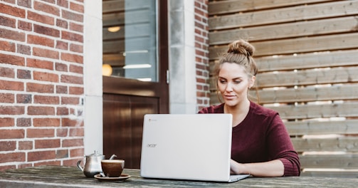 woman sitting and holding white Acer laptop near brown wooden wall