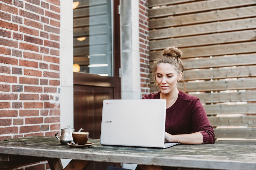 donna che si siede e tiene il computer portatile Acer bianco vicino al muro di legno marrone