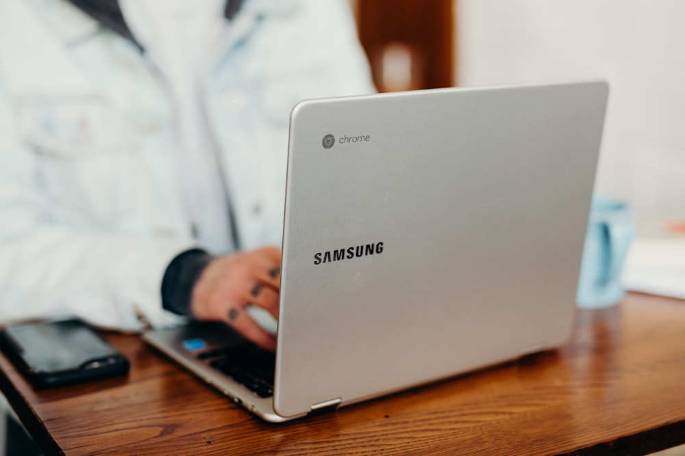 fotografía de enfoque superficial de una persona usando una computadora portátil Samsung gris