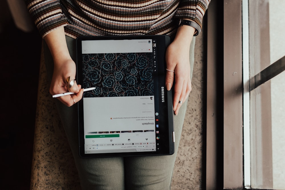 personne assise près d’un miroir en verre avec un écran d’ordinateur portable et tenant un stylet