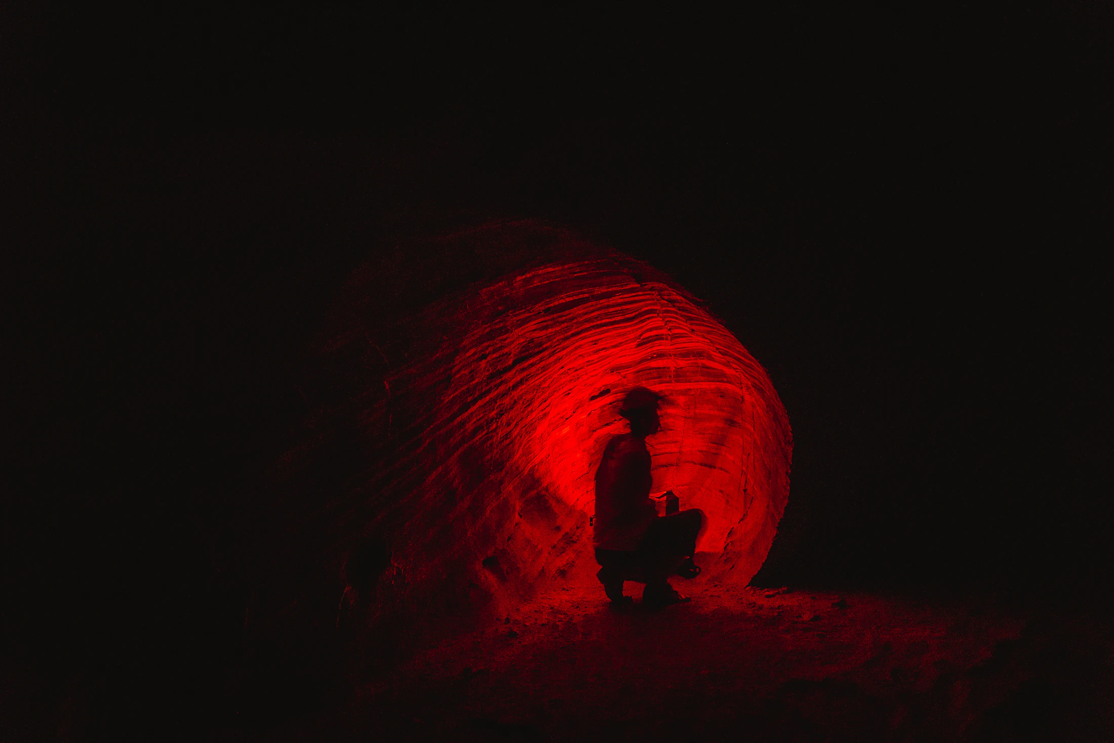 Explorateur dans une galerie rocheuse révélée par une lumière rouge.