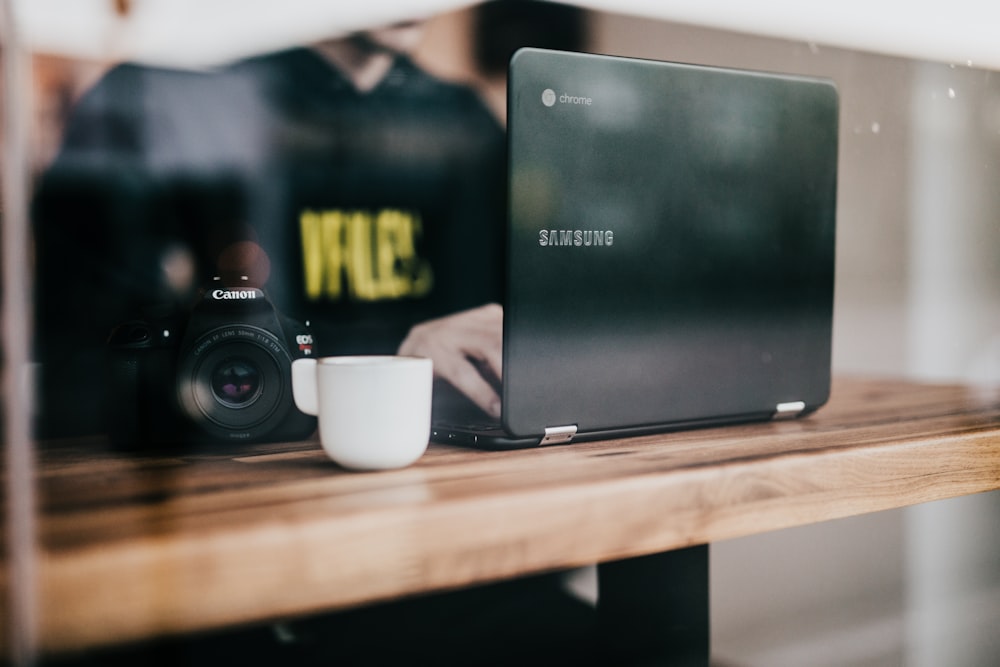 person using black Samsung laptop with cup and camera