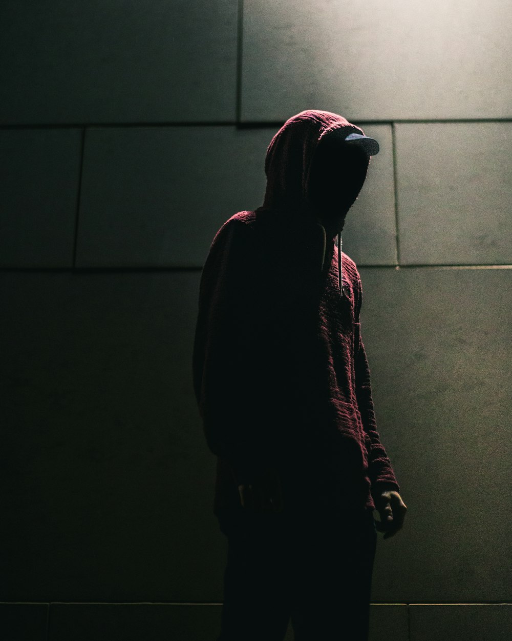 personne en sweat à capuche rouge debout devant un mur de briques grises