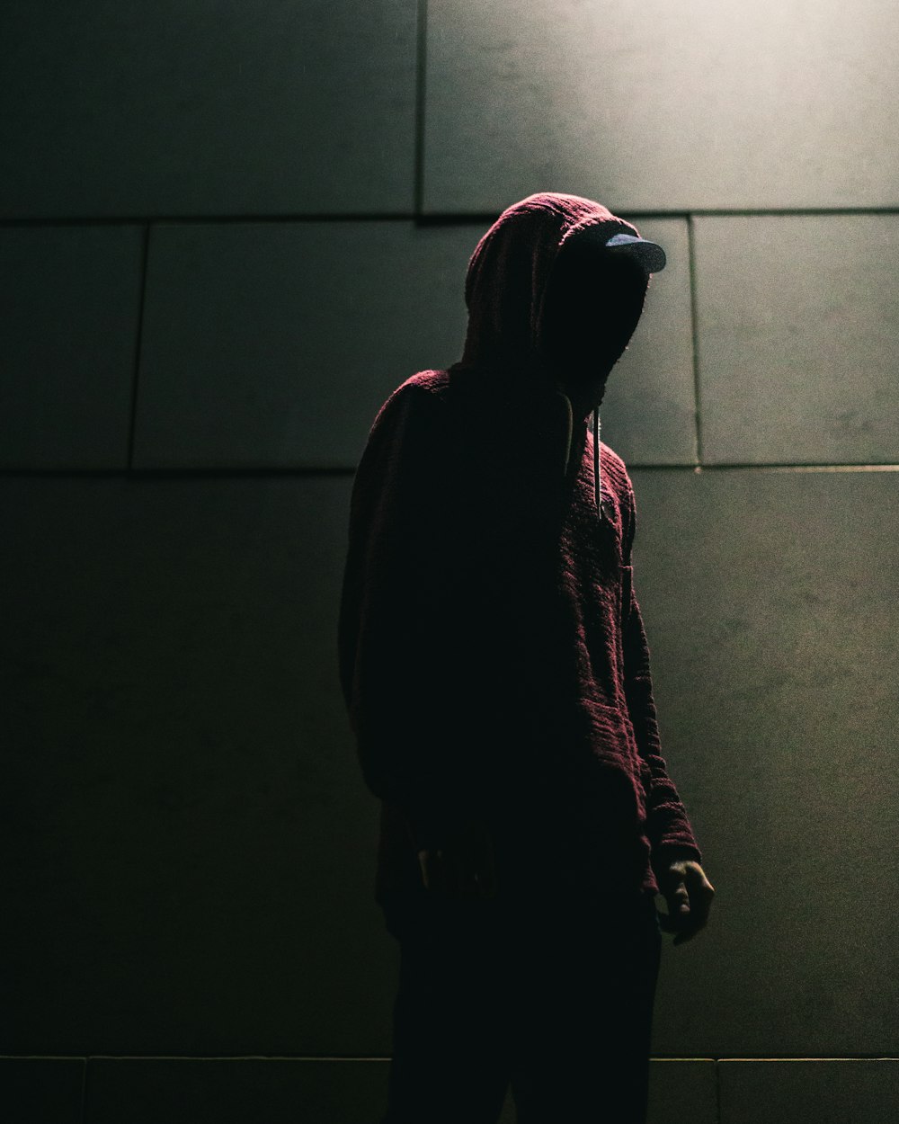 person in red hoodie standing in front of gray brick wall