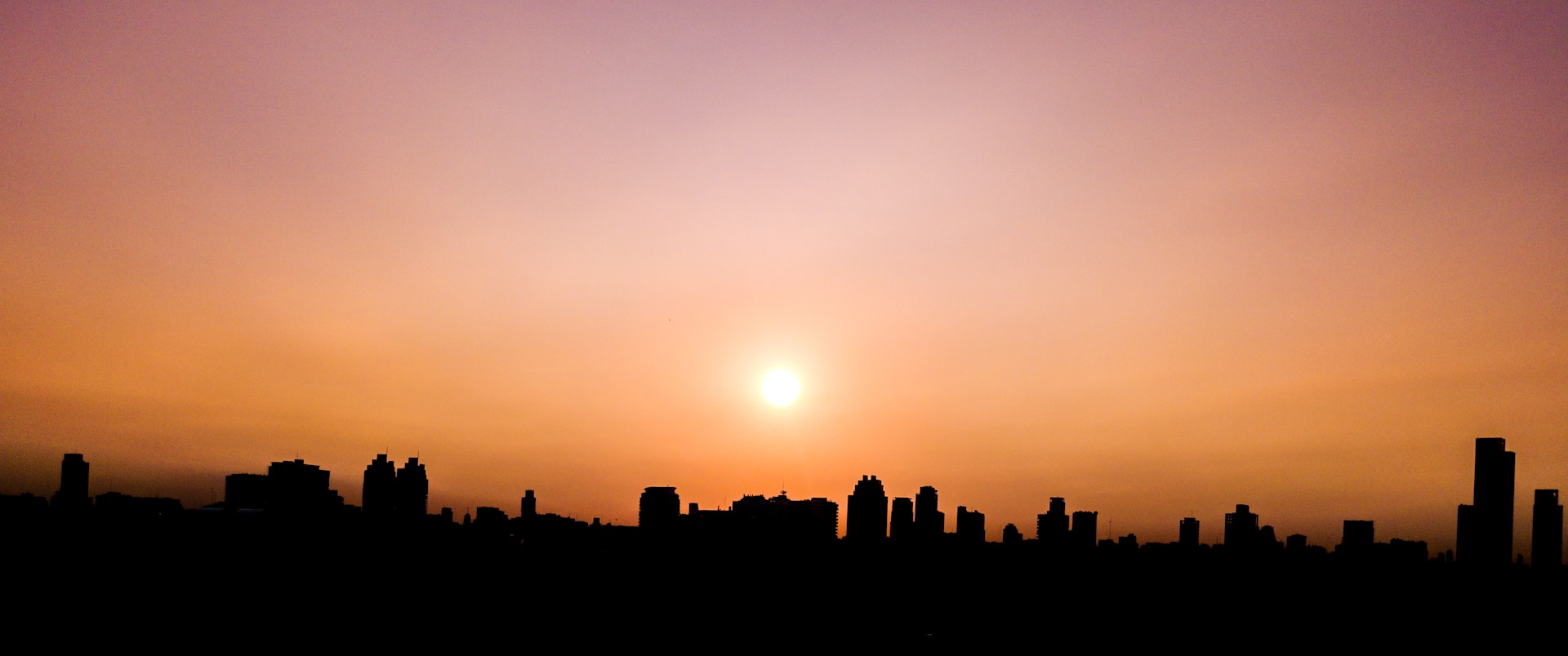A vibrant cityscape at sunset with warm orange and pink hues illuminating the skyline.