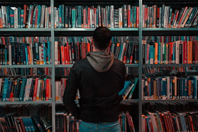 person wearing black and gray jacket in front of bookshelf