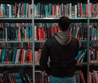 person wearing black and gray jacket in front of bookshelf