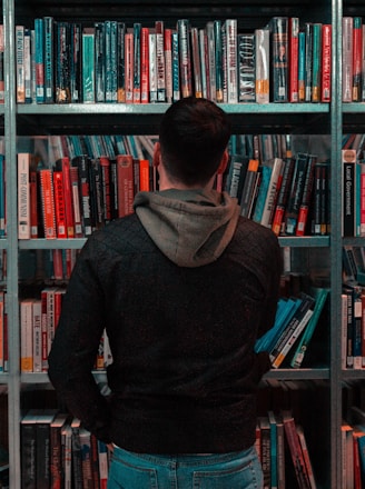 person wearing black and gray jacket in front of bookshelf