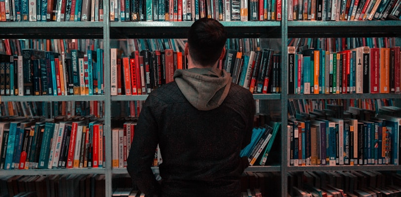 person wearing black and gray jacket in front of bookshelf