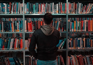 person wearing black and gray jacket in front of bookshelf