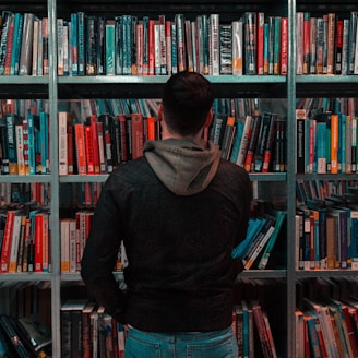 person wearing black and gray jacket in front of bookshelf