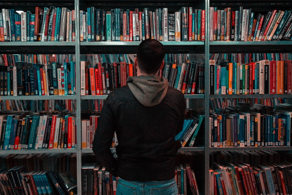 person wearing black and gray jacket in front of bookshelf