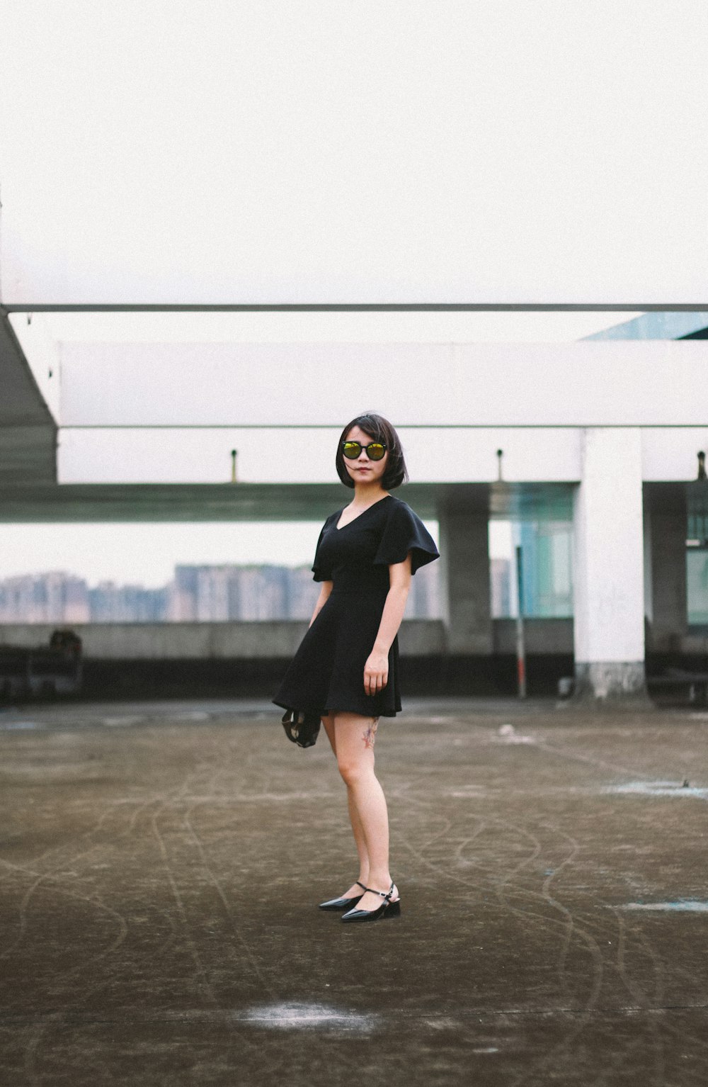 검은 미니 드레스와 검은 선글라스를 쓴 여자가 거리에 서 있습니다.