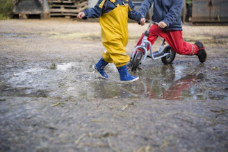 Kids wearing bright rain jackets and hats while exploring a muddy trail.