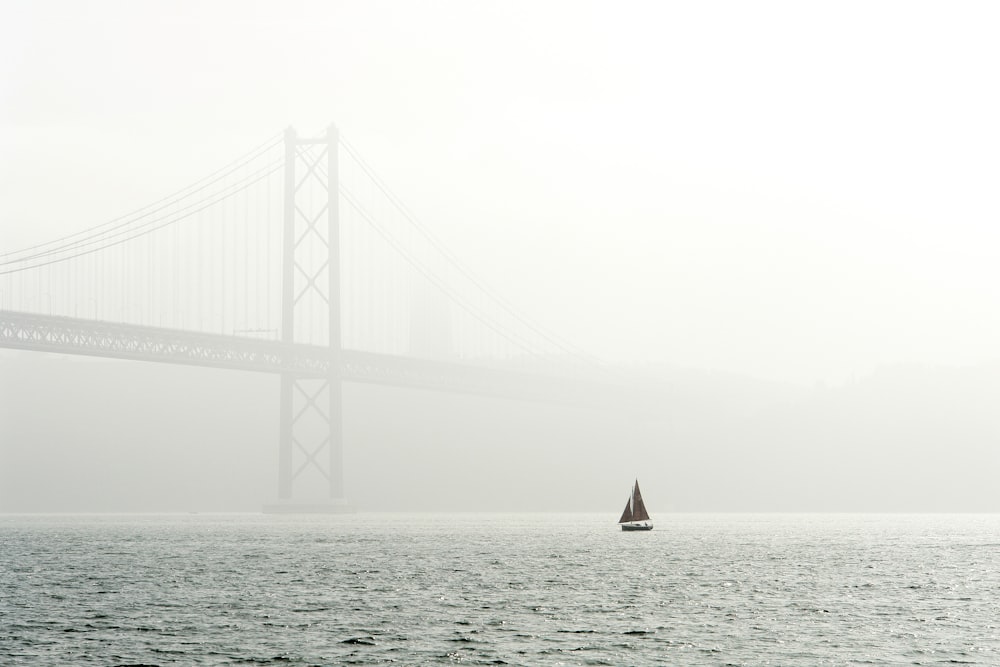barca a vela sullo specchio d'acqua vicino al ponte coperto dalla nebbia