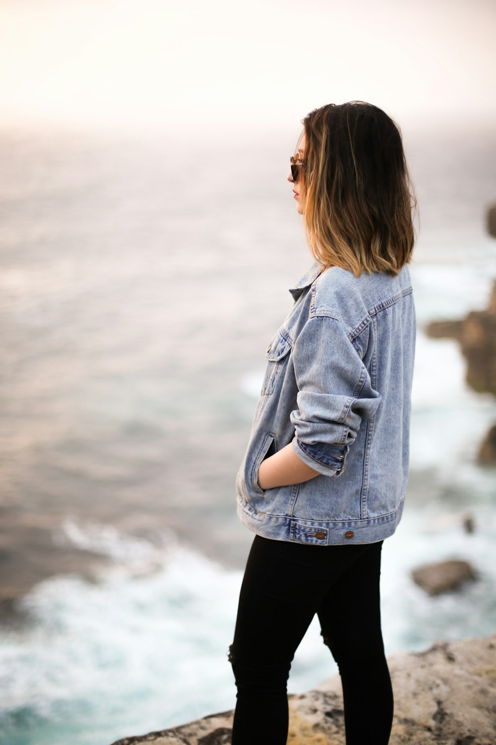 woman wearing blue denim jacket on cliff facing body of water