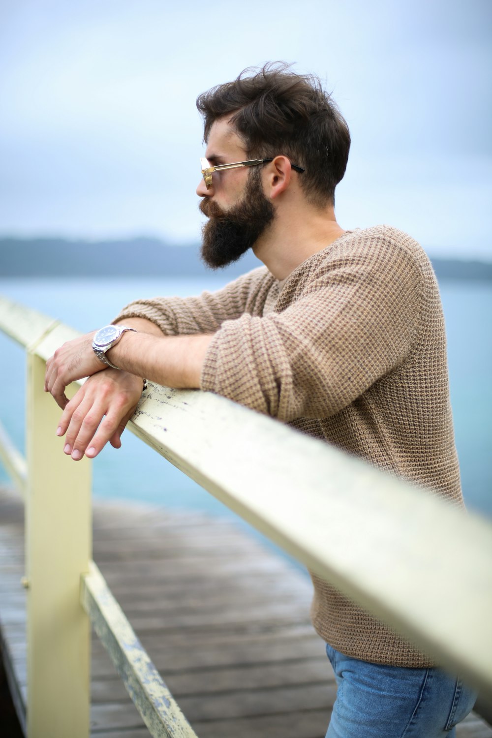 man wearing brown sweater standing on wooden dock
