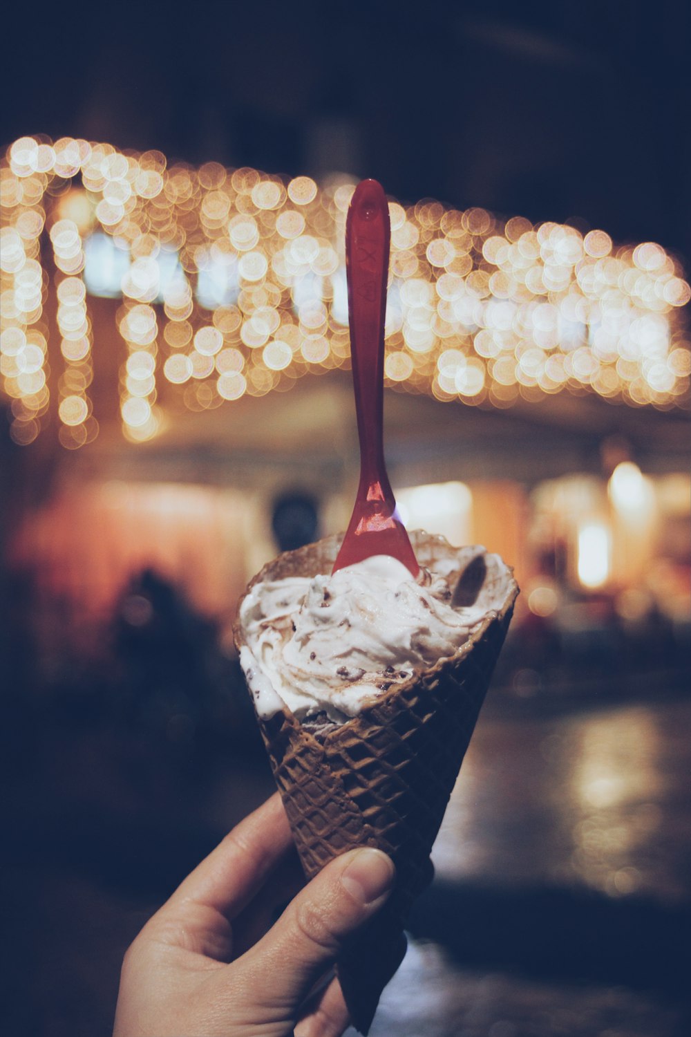 person holding sugar cone with white cream and plastic spoon