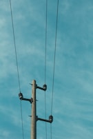 A tall utility pole with three electrical wires stretching across a clear sky. The pole is made of concrete and features several insulators.