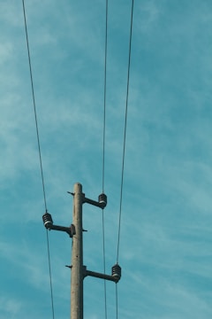 A tall utility pole with three electrical wires stretching across a clear sky. The pole is made of concrete and features several insulators.