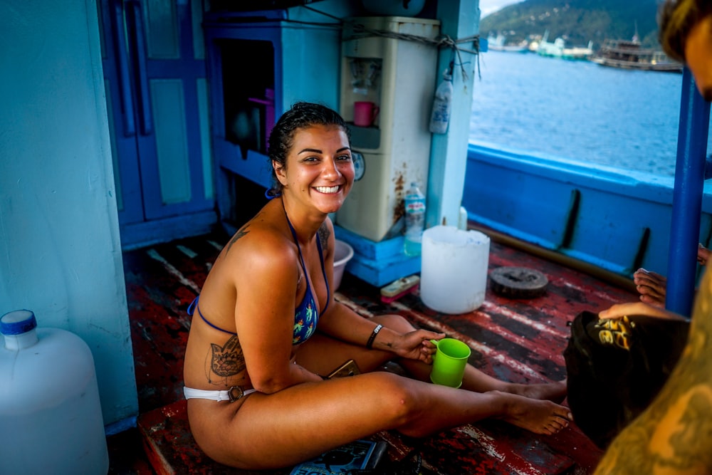 Frau im blauen Bikinioberteil hält grünen Becher, während sie im Boot sitzt